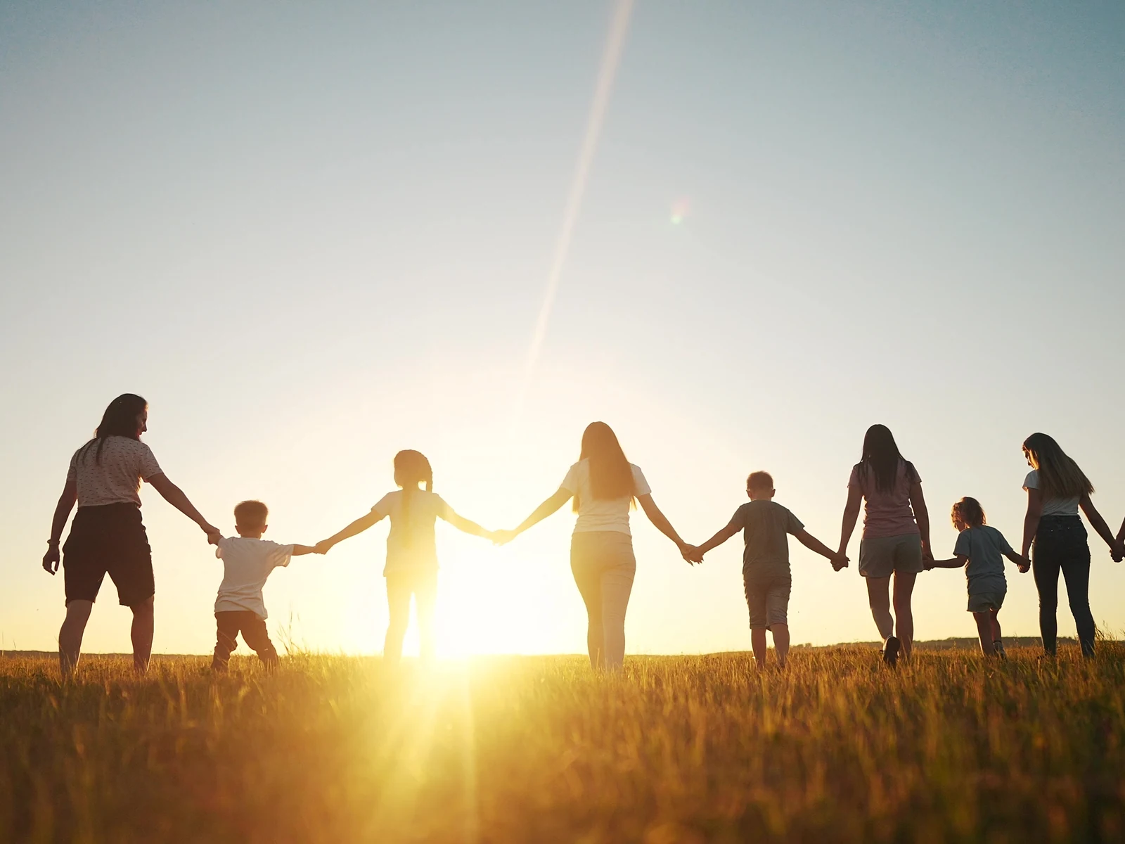 Menschen gehen Hand in Hand über eine Wiese in der Abendsonne