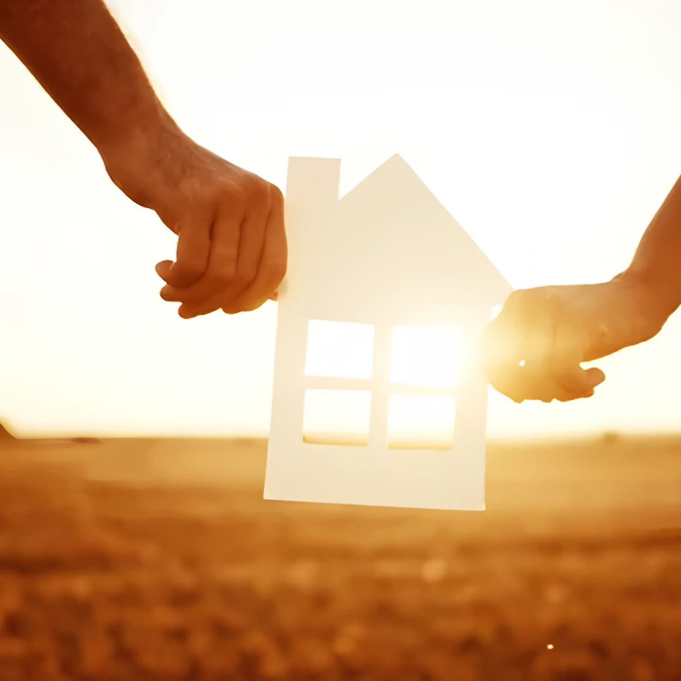 Zwei Hände halten ein Haus aus Papier vor der Abendsonne